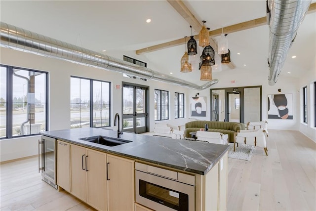 kitchen with a sink, a kitchen island with sink, open floor plan, beamed ceiling, and beverage cooler