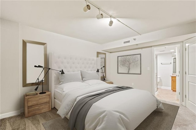 carpeted bedroom with track lighting, baseboards, and connected bathroom
