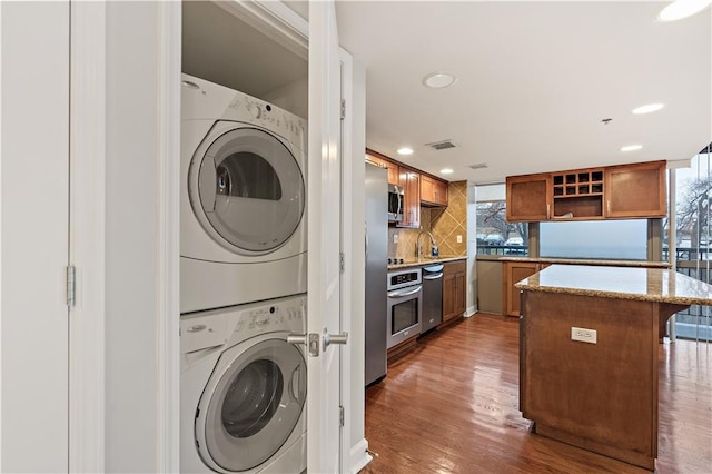 laundry room featuring stacked washer and clothes dryer, wood finished floors, and recessed lighting