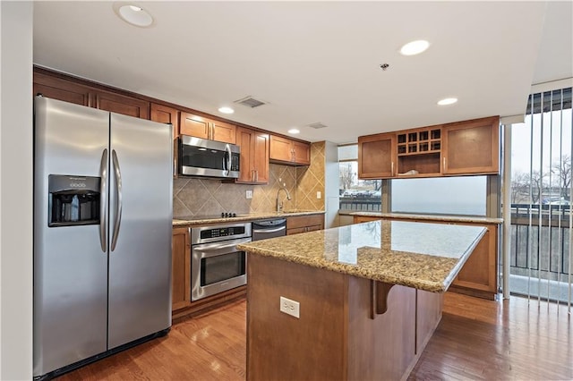 kitchen with appliances with stainless steel finishes, a kitchen island, wood finished floors, decorative backsplash, and recessed lighting