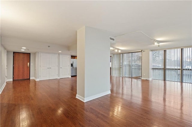 unfurnished living room featuring wood finished floors, rail lighting, and baseboards
