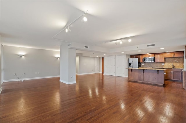unfurnished living room featuring rail lighting, dark wood-type flooring, baseboards, and a sink