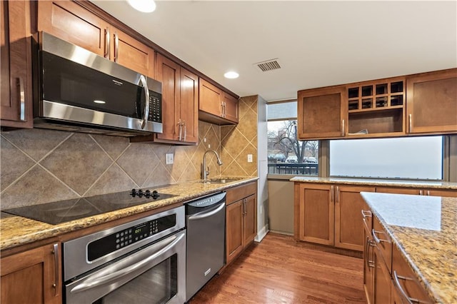 kitchen featuring stainless steel appliances, a sink, backsplash, open shelves, and wood finished floors