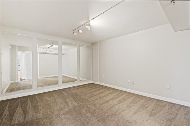 carpeted empty room featuring rail lighting and baseboards