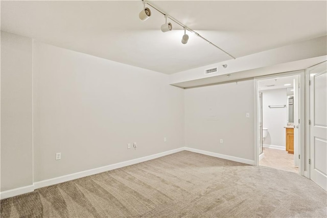 spare room featuring light carpet, rail lighting, and baseboards
