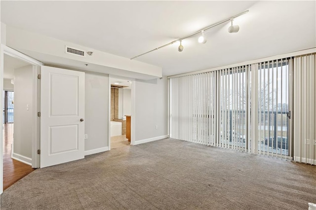 empty room with carpet, rail lighting, and baseboards