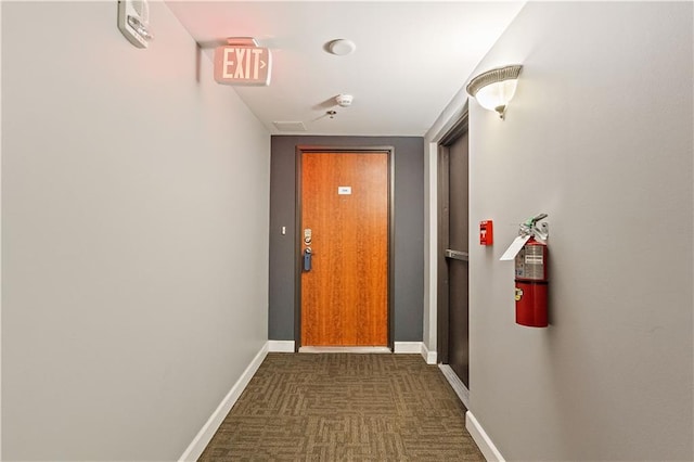 corridor with baseboards and dark carpet