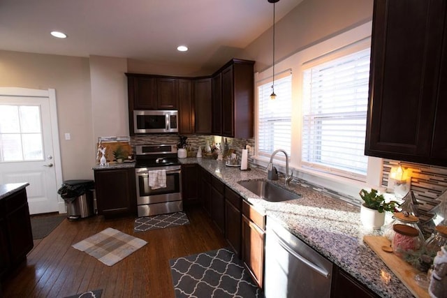 kitchen with a sink, stainless steel appliances, dark wood-type flooring, light stone countertops, and decorative backsplash