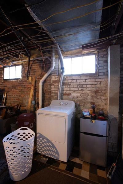 below grade area featuring brick wall, freestanding refrigerator, and washer / dryer