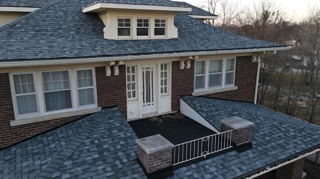 rear view of house with roof with shingles and brick siding
