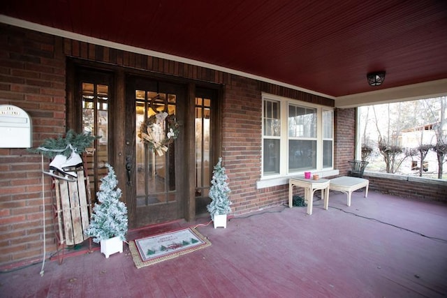 view of exterior entry with a porch and brick siding