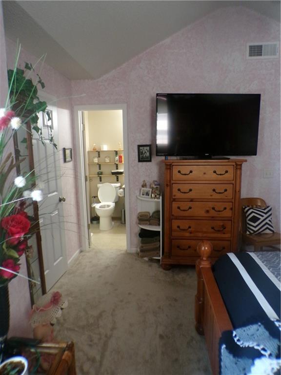 bedroom with vaulted ceiling, light carpet, ensuite bathroom, and visible vents