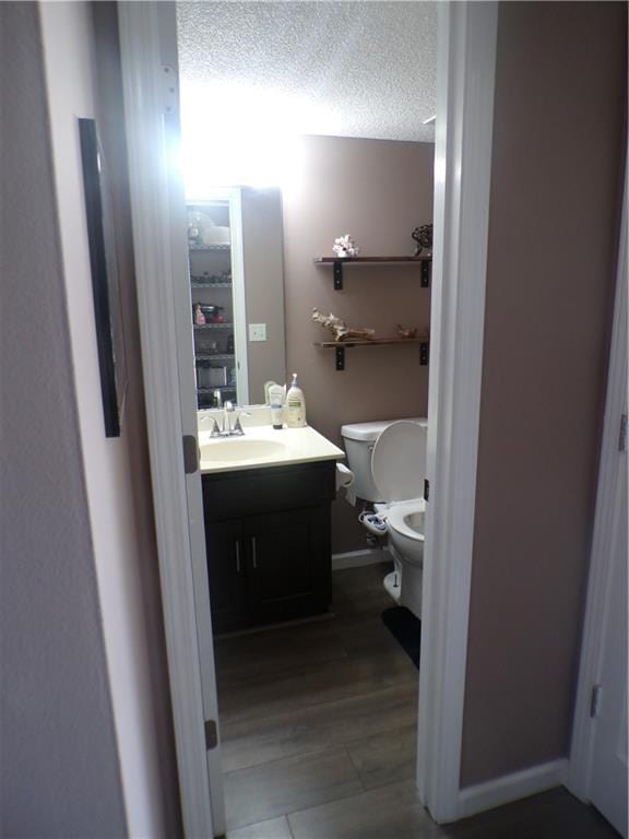 half bath with toilet, baseboards, vanity, and a textured ceiling
