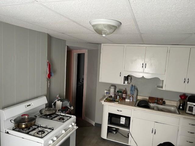 kitchen with white gas range, light countertops, white cabinets, and a sink