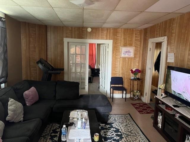 living room with ceiling fan, wooden walls, and a drop ceiling