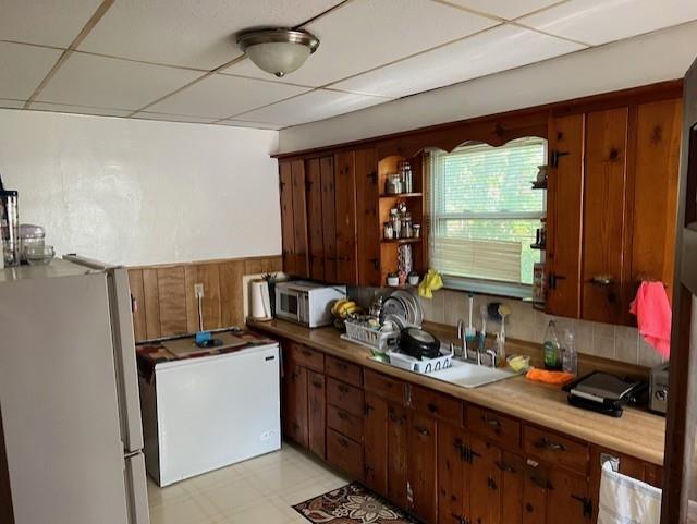 kitchen featuring a drop ceiling, refrigerator, a sink, freestanding refrigerator, and open shelves
