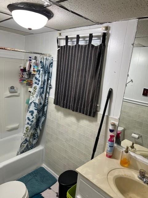 full bath featuring toilet, shower / bath combo with shower curtain, tile patterned floors, tile walls, and vanity