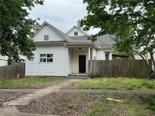 bungalow-style home with a shingled roof, a chimney, and fence