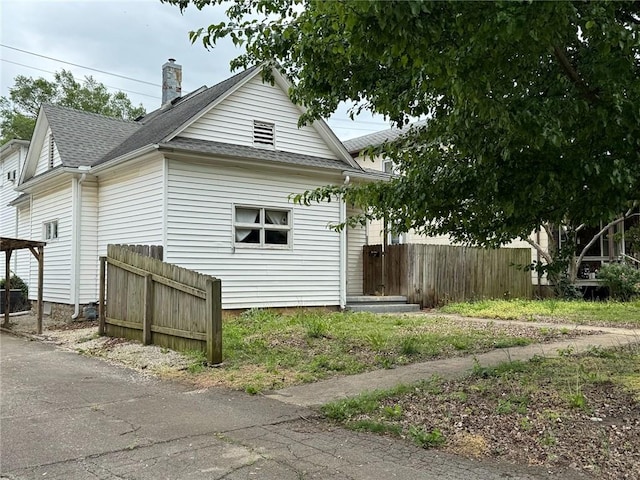 view of side of home with a chimney, a shingled roof, and fence