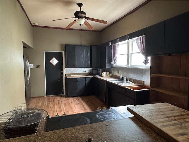 kitchen featuring freestanding refrigerator, light wood-type flooring, black microwave, a ceiling fan, and dark cabinetry