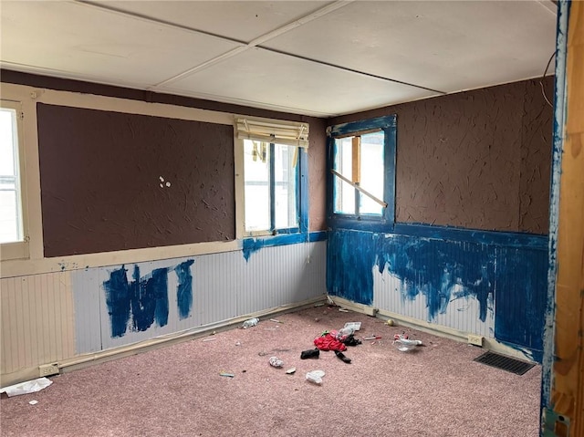 empty room featuring carpet flooring, visible vents, wainscoting, and a textured wall