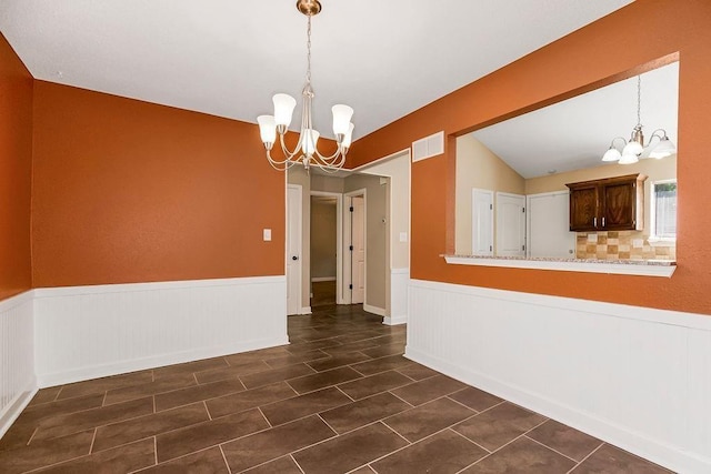 unfurnished dining area featuring a chandelier, wainscoting, dark tile patterned flooring, and lofted ceiling
