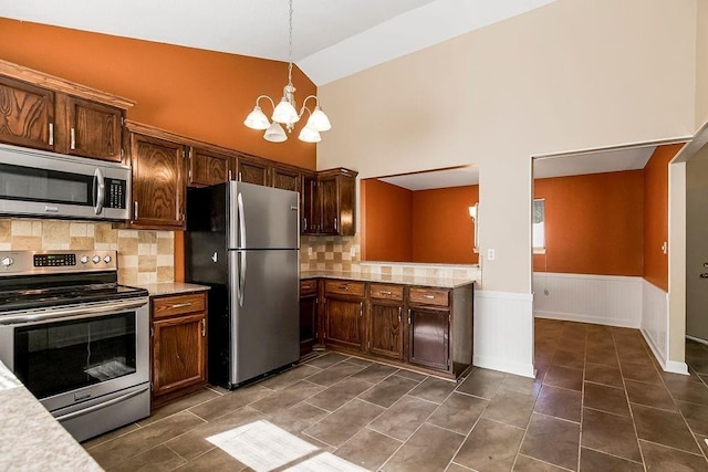 kitchen featuring appliances with stainless steel finishes, a chandelier, a wainscoted wall, decorative light fixtures, and dark tile patterned flooring