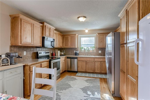 8403 NE 115th Ter, Kansas City, MO 64157 - kitchen featuring stainless steel appliances, light wood-type flooring, light countertops, tasteful backsplash, and a textured ceiling