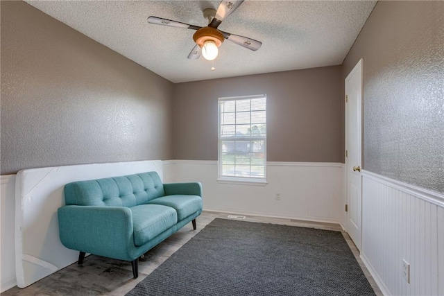 8403 NE 115th Ter, Kansas City, MO 64157 - living area with a textured ceiling, a ceiling fan, wainscoting, and a textured wall