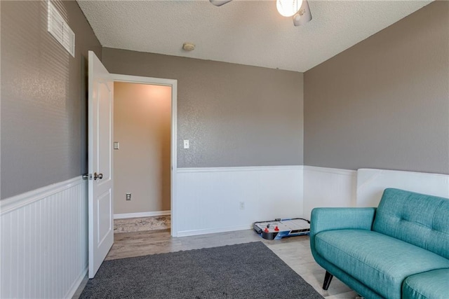 8403 NE 115th Ter, Kansas City, MO 64157 - living area featuring a wainscoted wall, a ceiling fan, wood finished floors, and a textured ceiling