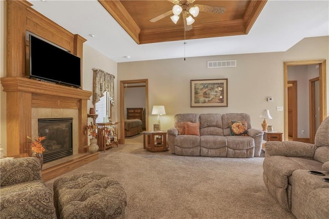 carpeted living room featuring a raised ceiling, a ceiling fan, crown molding, and a tiled fireplace