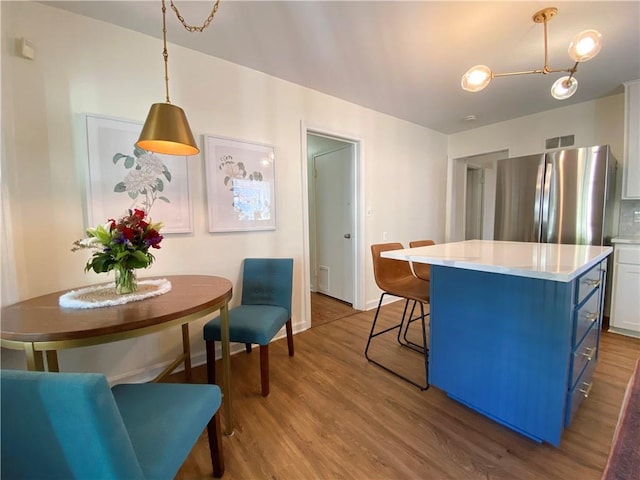 kitchen featuring freestanding refrigerator, blue cabinets, wood finished floors, light countertops, and a kitchen breakfast bar