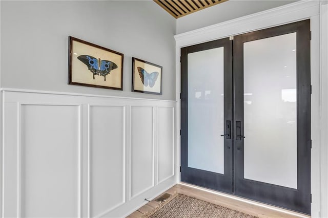 doorway featuring a decorative wall, french doors, a wainscoted wall, and wood finished floors