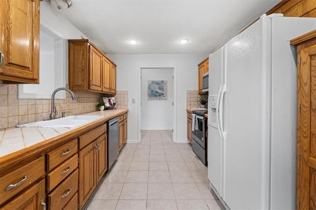 7955 W 118th Pl, Overland Park, KS 66210 - kitchen featuring stainless steel appliances, tile counters, brown cabinetry, decorative backsplash, and light tile patterned flooring