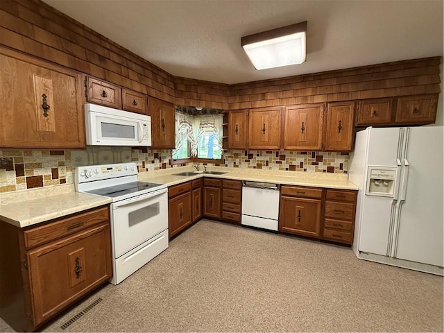 kitchen featuring a sink, brown cabinetry, white appliances, and tasteful backsplash