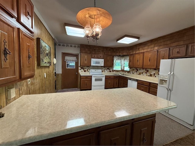 kitchen featuring a peninsula, wood walls, white appliances, light countertops, and tasteful backsplash