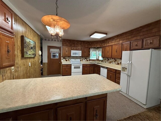 kitchen featuring a sink, wooden walls, white appliances, light countertops, and a chandelier