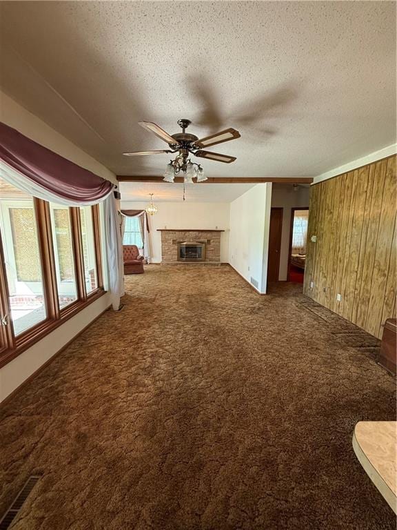unfurnished living room with a ceiling fan, carpet, a textured ceiling, visible vents, and wood walls