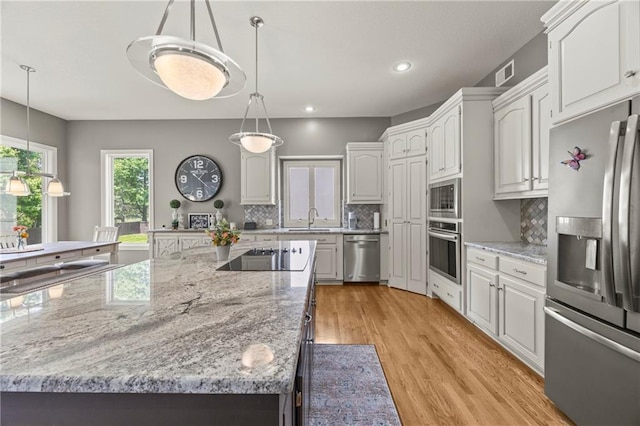 14692 S Garnett St, Olathe, KS 66062 - kitchen featuring stainless steel appliances, tasteful backsplash, light wood-style flooring, white cabinets, and decorative light fixtures