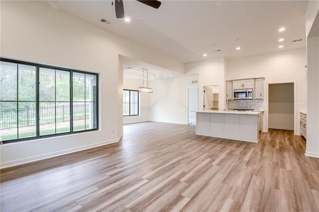 unfurnished living room with ceiling fan, baseboards, visible vents, and light wood-style floors