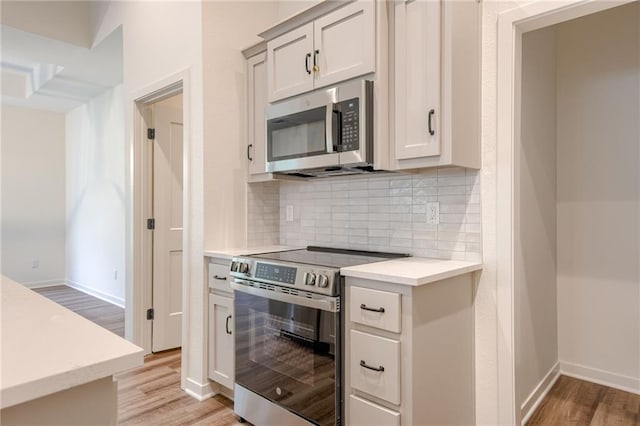 kitchen with baseboards, light wood finished floors, decorative backsplash, light countertops, and appliances with stainless steel finishes