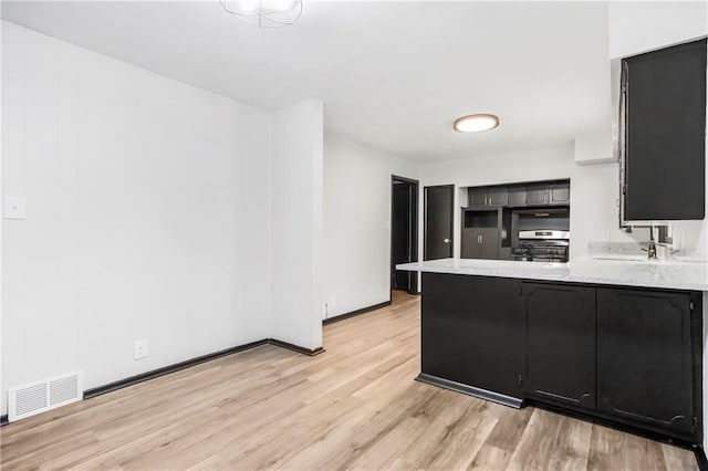 1910 Ottawa St, Leavenworth, KS 66048 - kitchen featuring stainless steel stove, dark cabinetry, a peninsula, light wood-style floors, and light countertops