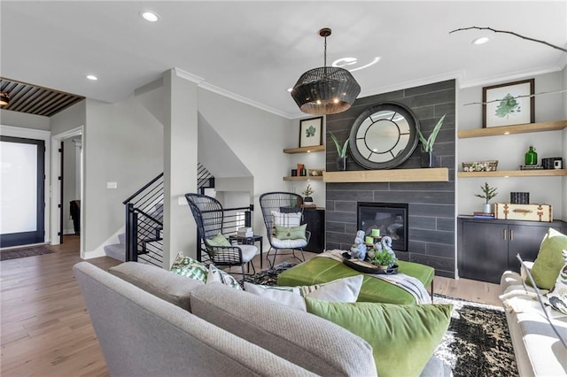 living area featuring wood finished floors, a tiled fireplace, crown molding, baseboards, and stairs