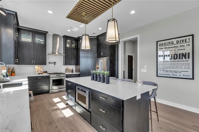 kitchen with stainless steel appliances, dark cabinets, light wood-type flooring, and wall chimney exhaust hood