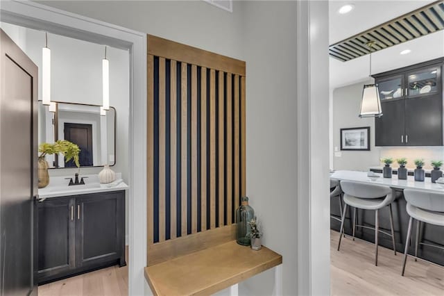 interior space with glass insert cabinets, a sink, light countertops, light wood-style floors, and dark cabinetry