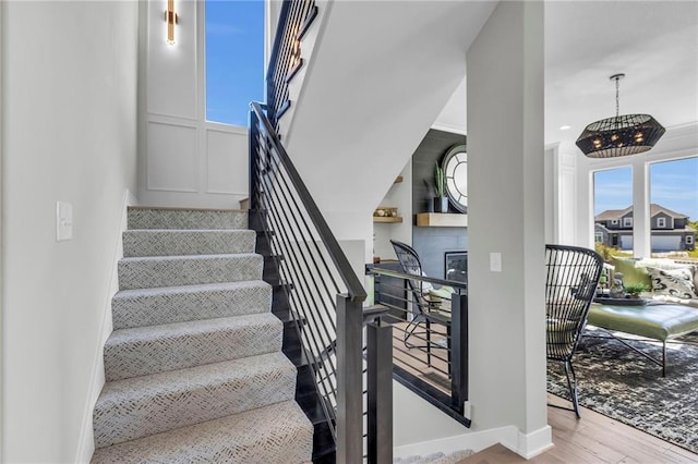 stairs featuring an inviting chandelier, wood finished floors, baseboards, and a fireplace