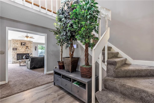 stairway with carpet, wood finished floors, a fireplace, baseboards, and ceiling fan
