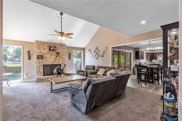 living room featuring lofted ceiling, light colored carpet, a textured ceiling, ceiling fan, and a stone fireplace