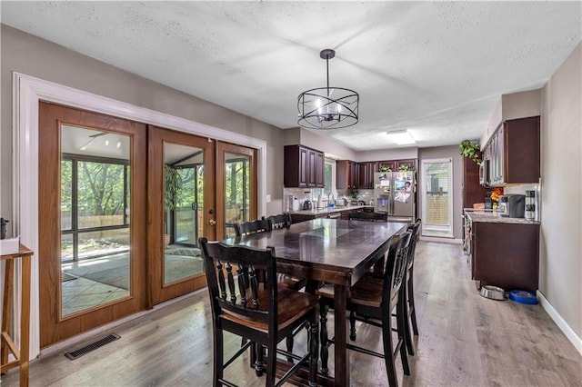 dining area with french doors, a textured ceiling, light wood-type flooring, visible vents, and a chandelier