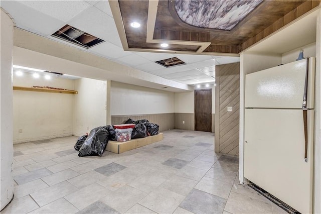 finished below grade area featuring freestanding refrigerator, a paneled ceiling, wainscoting, and wood walls